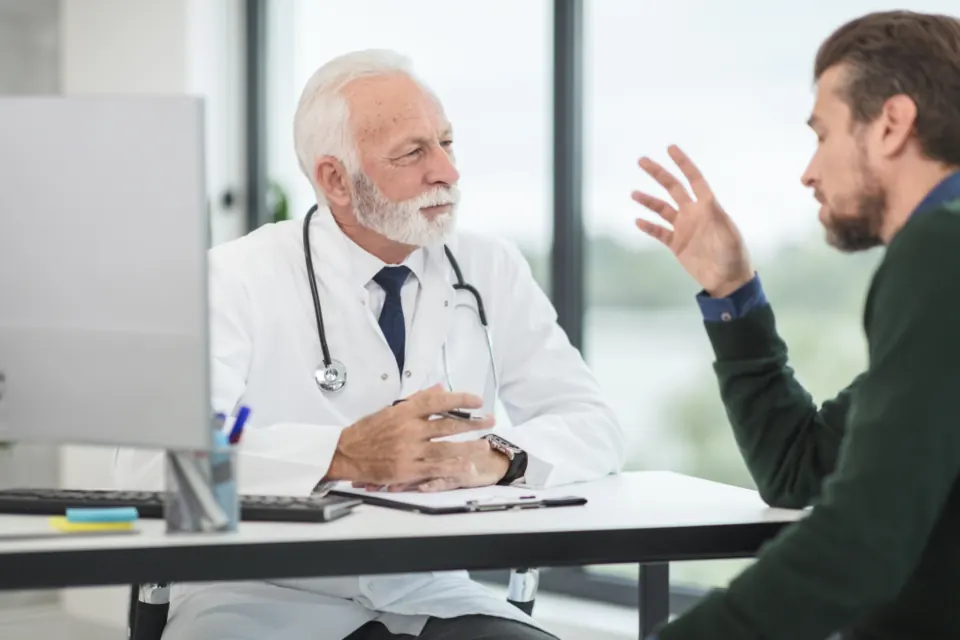 A physician and a client talking across a desk in a bright consultation room