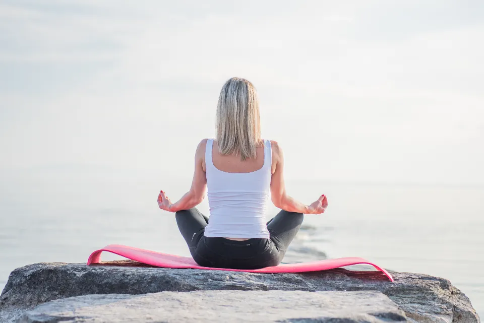 A woman meditating on a rock by the sea