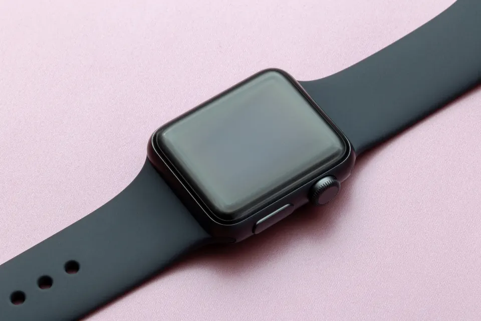 A smartwatch with a dark band on a pink surface
